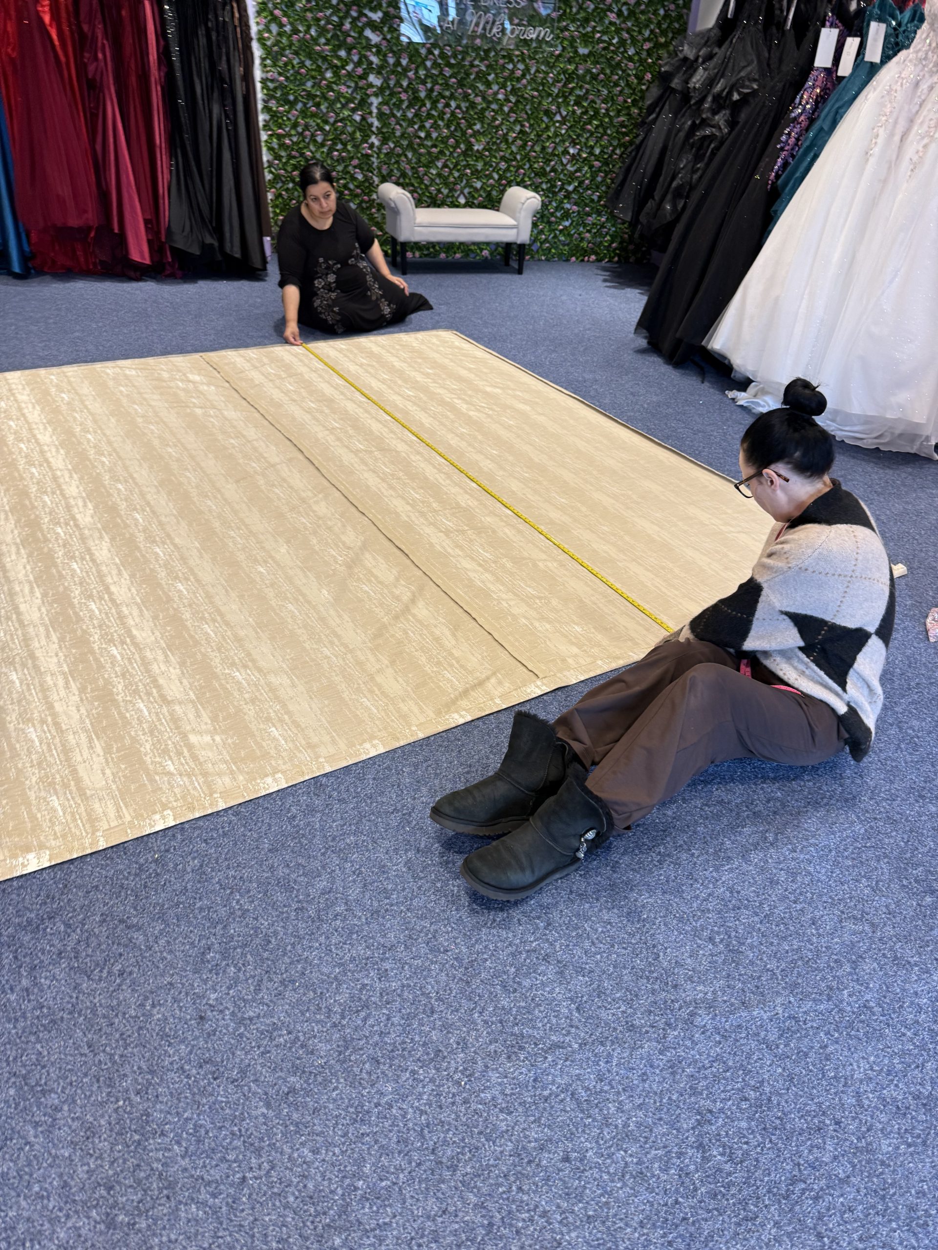 Two MK Seamstress team members measuring a large gold curtain panel for alterations